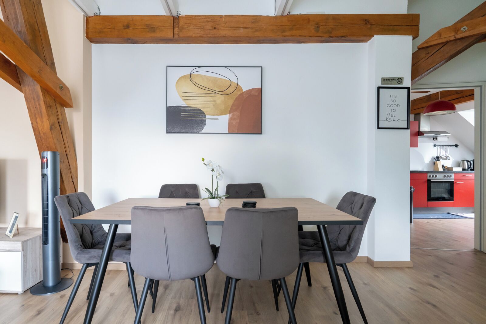 Un coin repas avec une table en bois, des chaises à revêtement gris et un tableau abstrait moderne accroché au mur.