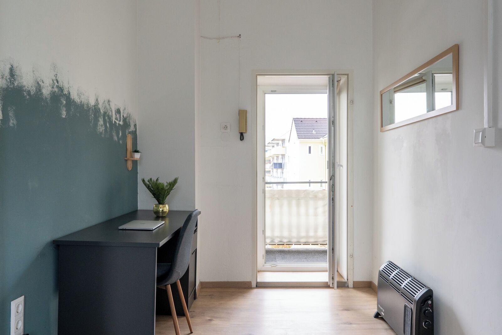 A narrow hallway with a desk, chair, and radiator. A door leads to an outdoor balcony.