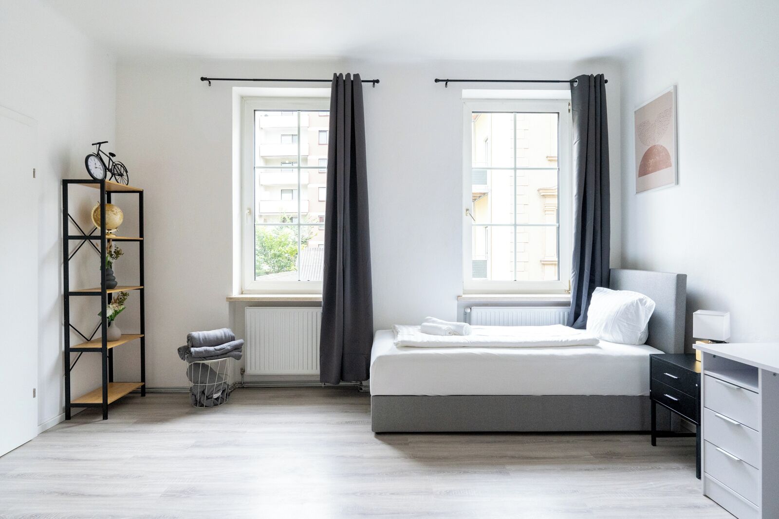 Ett minimalistiskt sovrum med en säng, ett element, ett fönster med gardiner, en hylla med en jordglob och ett elementöverdrag.