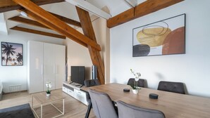 A modern living room with a wooden ceiling, a dining table with chairs, a TV, and a painting on the wall. - COY Apartments Leoben - Stay Comfortable & Work Smart (Leoben)