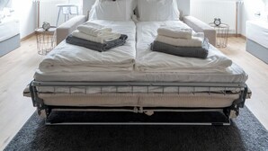 A loft bedroom with a high ceiling, exposed wooden beams, a large bed with neatly folded blankets, and a view of the outside through a window. - COY Apartments Leoben - Stay Comfortable & Work Smart (Leoben)
