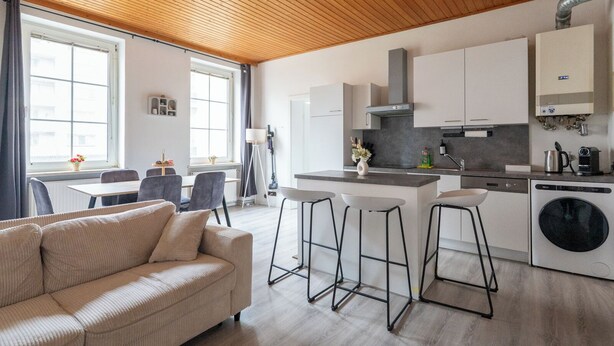 A modern kitchen with white cabinets, a central island, and a built-in washing machine. - COY Apartments Leoben - Stay Comfortable & Work Smart (Leoben)