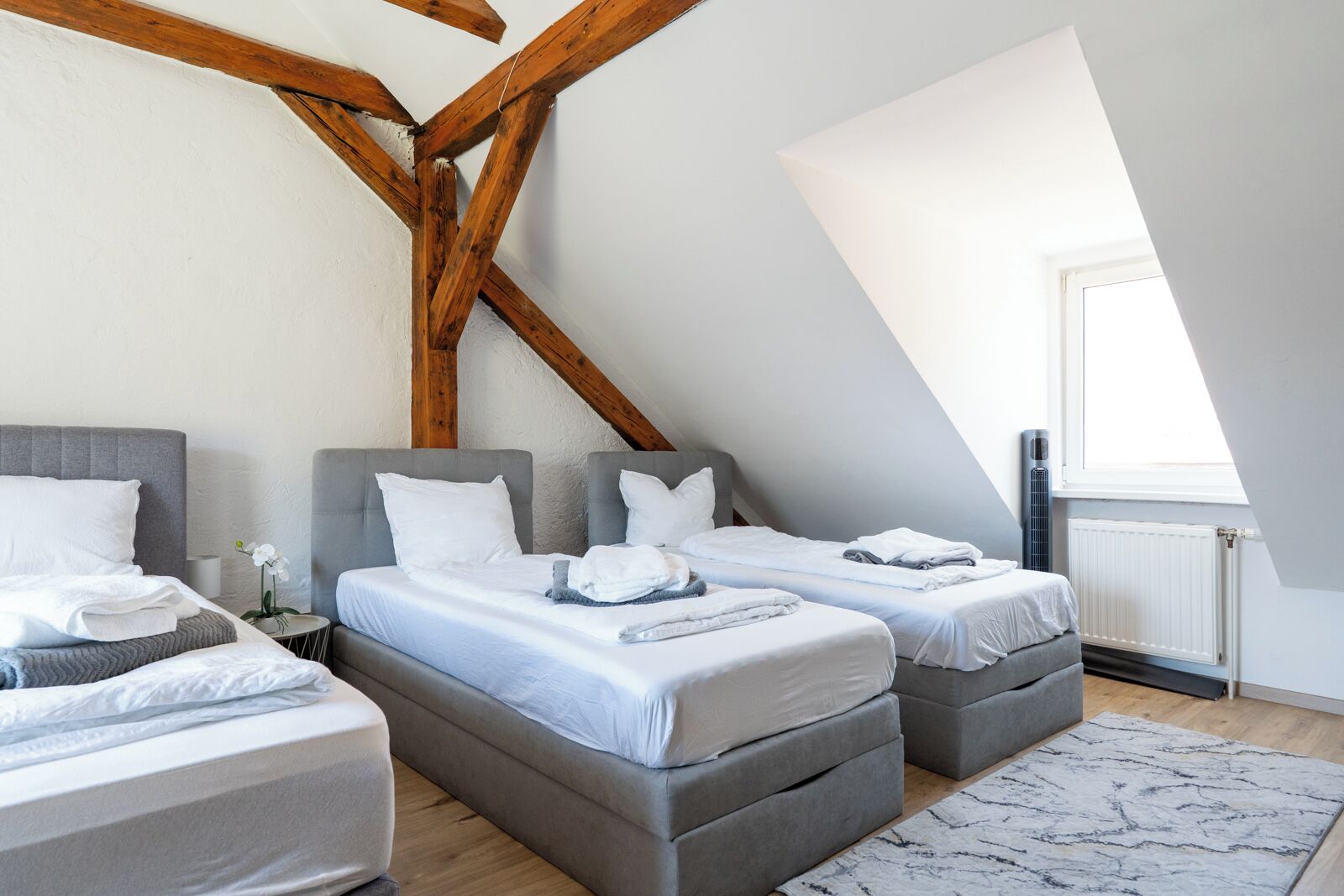 Une chambre avec deux lits, un plafond en bois, un radiateur et une fenêtre.
