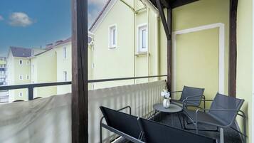 En balkon med to stole og et lille bord, med udsigt over en række gule bygninger.