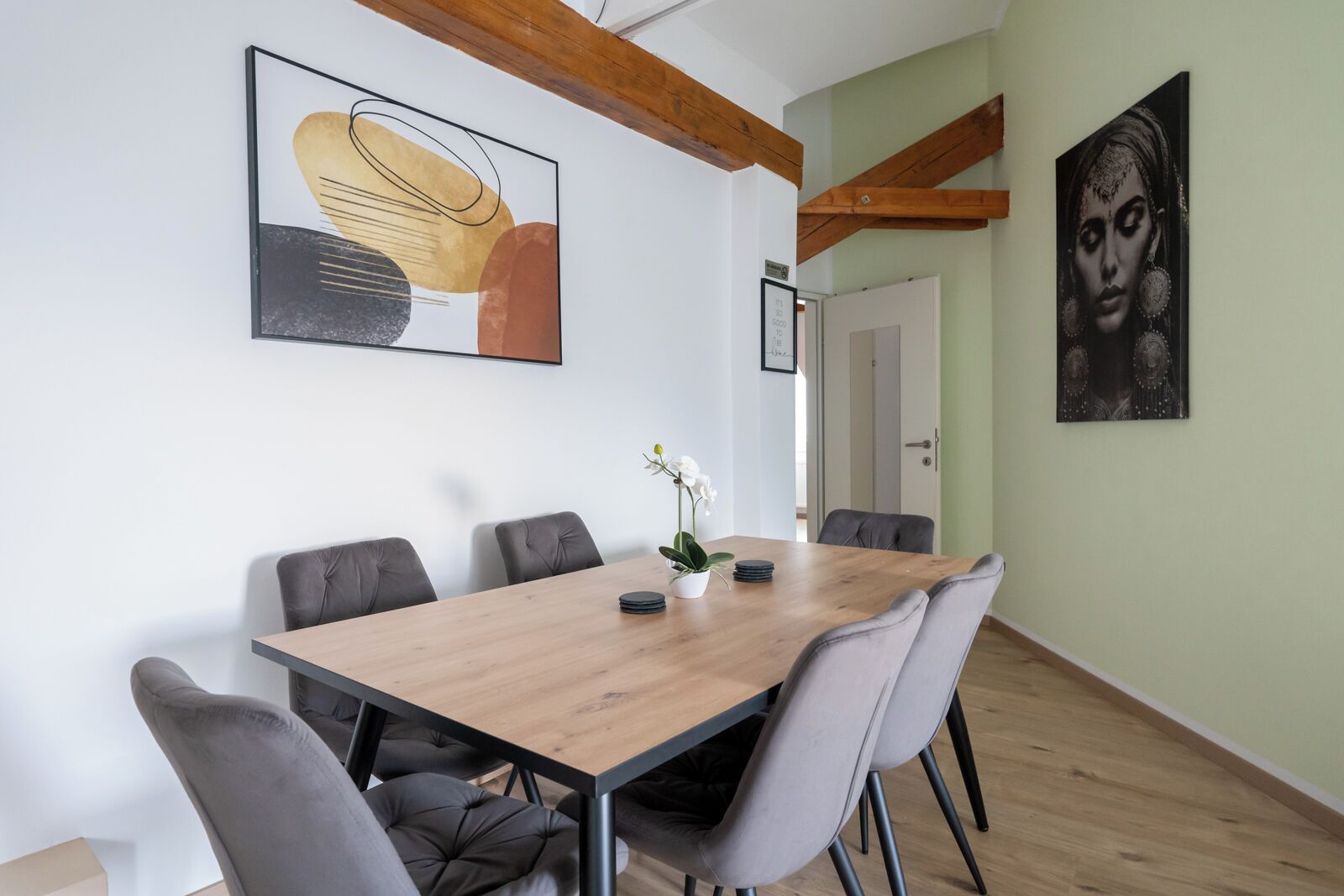 Ein Essbereich mit einem Holztisch, grau gepolsterten Stühlen und einer Vase mit weißen Blumen.