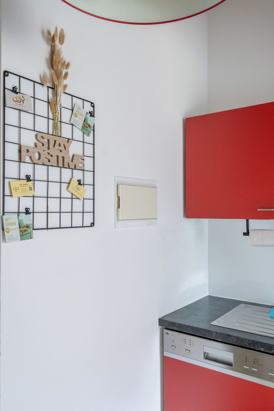 A kitchen with a red cabinet, a white wall with a bulletin board, and a coffee machine.