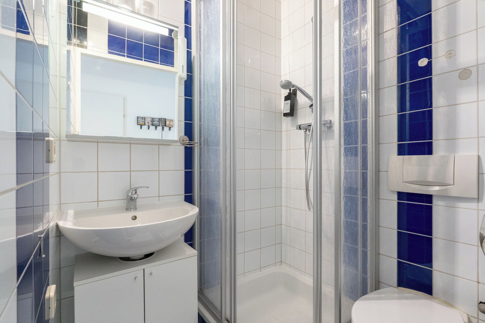 Ein modernes Badezimmer mit einem weißen Waschbecken, einer Duschkabine und blauen Fliesenwänden.