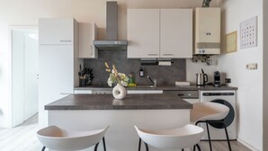 A modern kitchen with white cabinets, a central island with stools, and a stainless steel range hood. - COY Apartments Leoben - Stay Comfortable & Work Smart (Leoben)