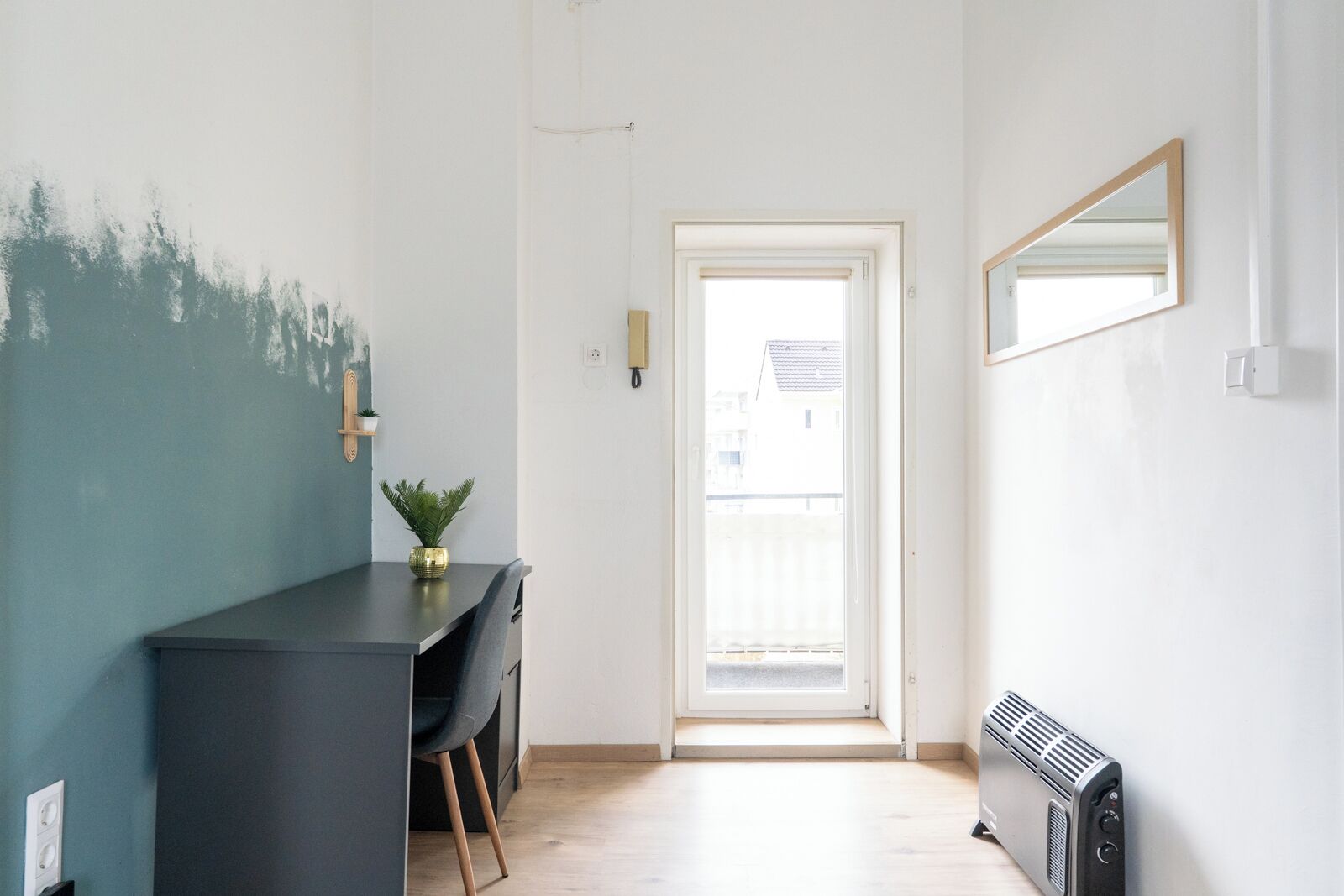 A modern interior with a dark-colored desk, a potted plant, a radiator, and a door leading to an outdoor area.