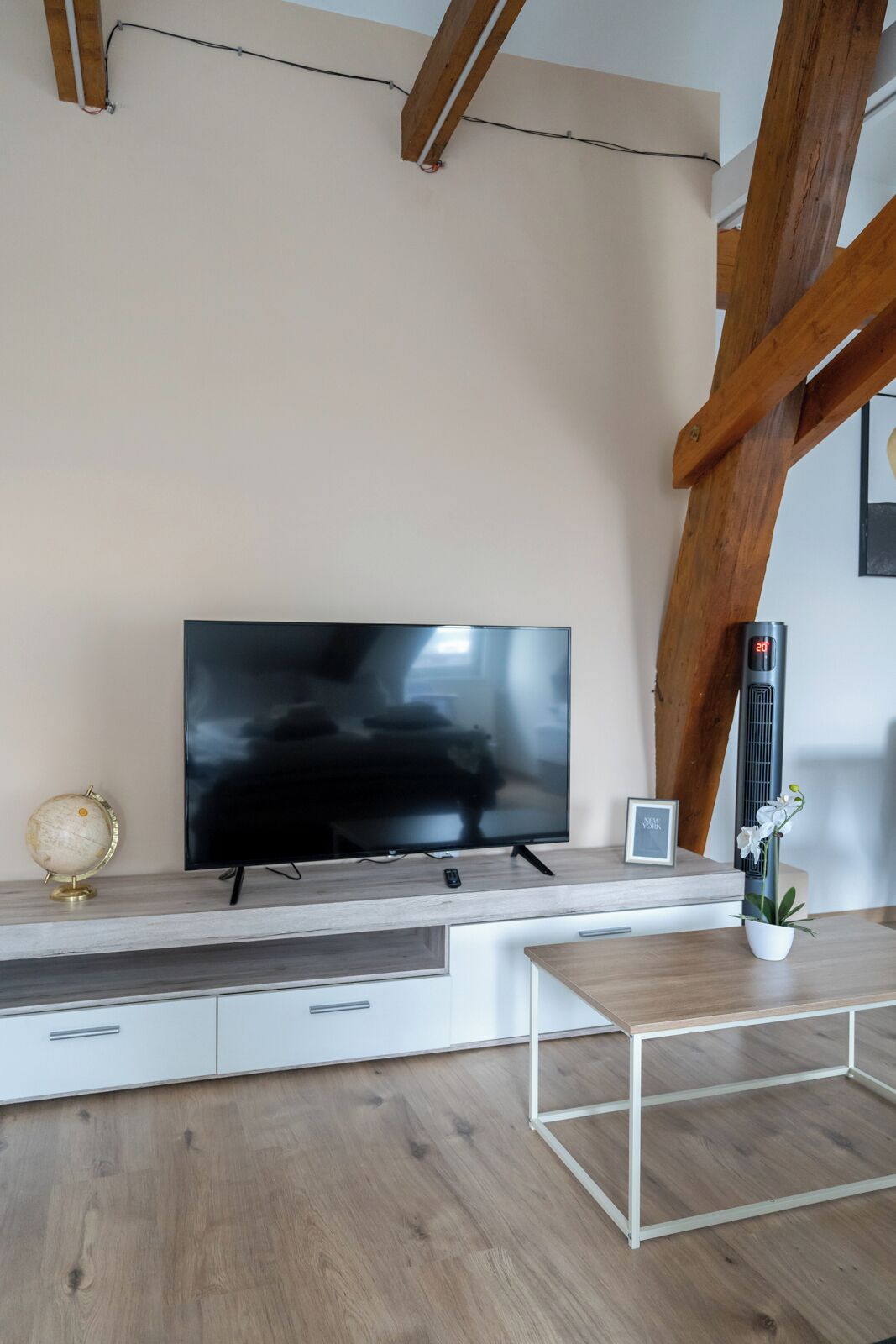 Uma sala de estar moderna com uma TV de tela plana em uma prateleira de madeira, um globo pequeno, um quadro emoldurado e uma orquídea em vaso.
