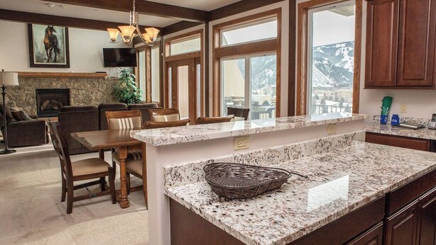 Une cuisine spacieuse dotée de plans de travail en granit, d’armoires en bois et de grandes fenêtres offrant une vue sur les montagnes.
