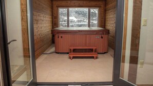 Une cabane en bois avec un bain à remous, une fenêtre donnant sur un paysage enneigé et un banc.