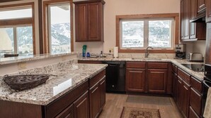 Une cuisine dotée de meubles en bois, de plans de travail en granit et offrant une vue sur des montagnes enneigées grâce à de grandes fenêtres.