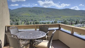 Un balcon avec une table ronde et quatre chaises, offrant une vue panoramique sur les montagnes et un lac.