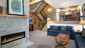 A spacious living room with a fireplace, a blue sofa, a wooden coffee table, and a staircase leading to an upper level. - Wonderful Mountain Home, Hot Tub, Complimentary Shuttle to Slopes (Beaver Creek)