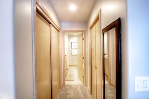 A narrow hallway with wooden doors on both sides, leading to a bathroom with a shower and toilet visible in the background.