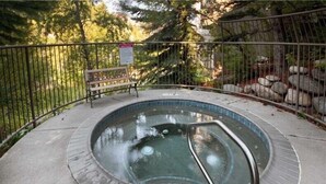 A hot tub with a metal railing, surrounded by a metal fence, with a bench and a sign in the background. - Updated with a Modern Touch, Hot Tub, on the Eagle River (Avon)