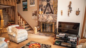 Tunnelmallinen olohuone, jossa on takka, televisio ja portaat, jotka johtavat ylempään kerrokseen.