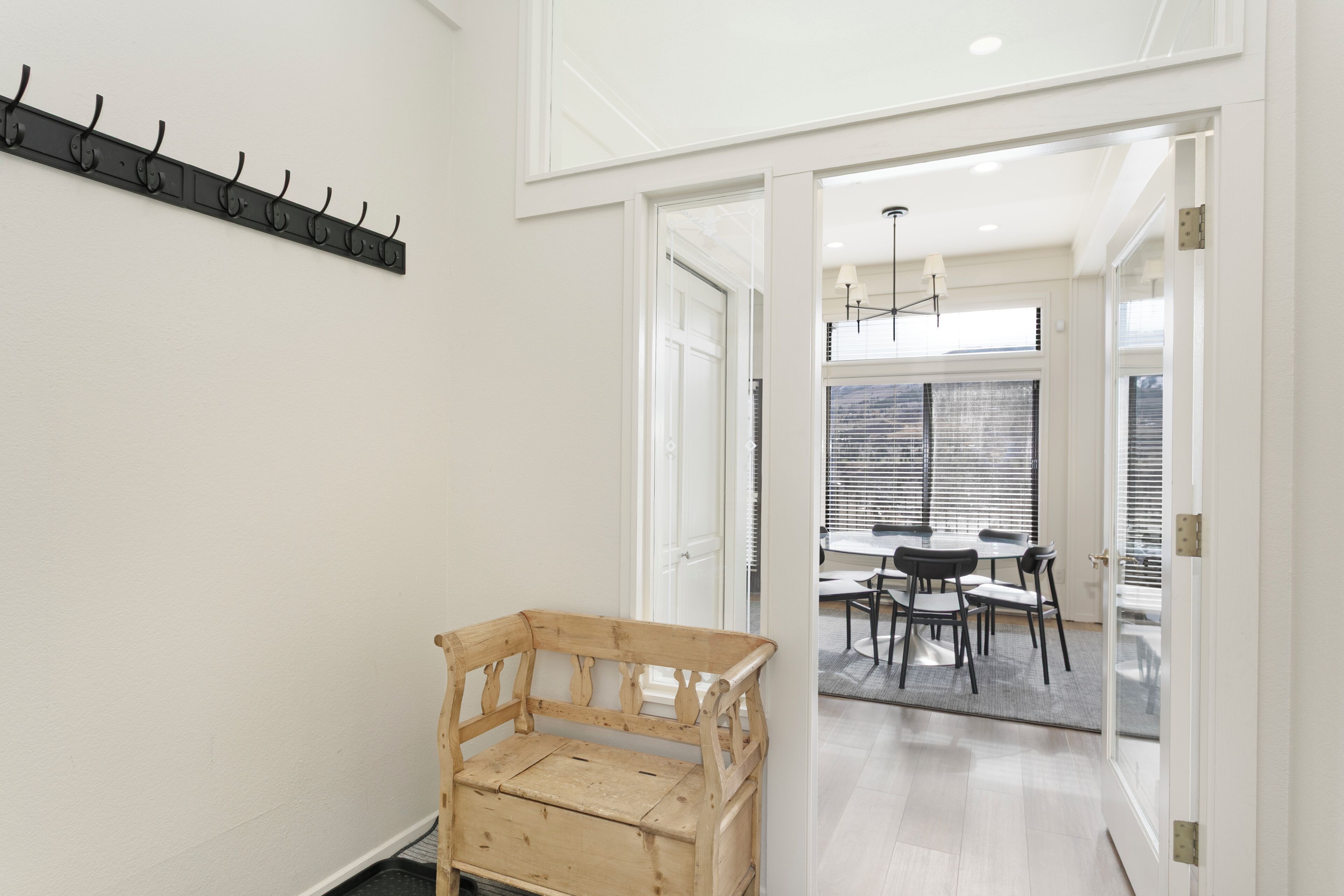 A room with a wooden bench, a coat rack, and a dining area with a table and chairs.