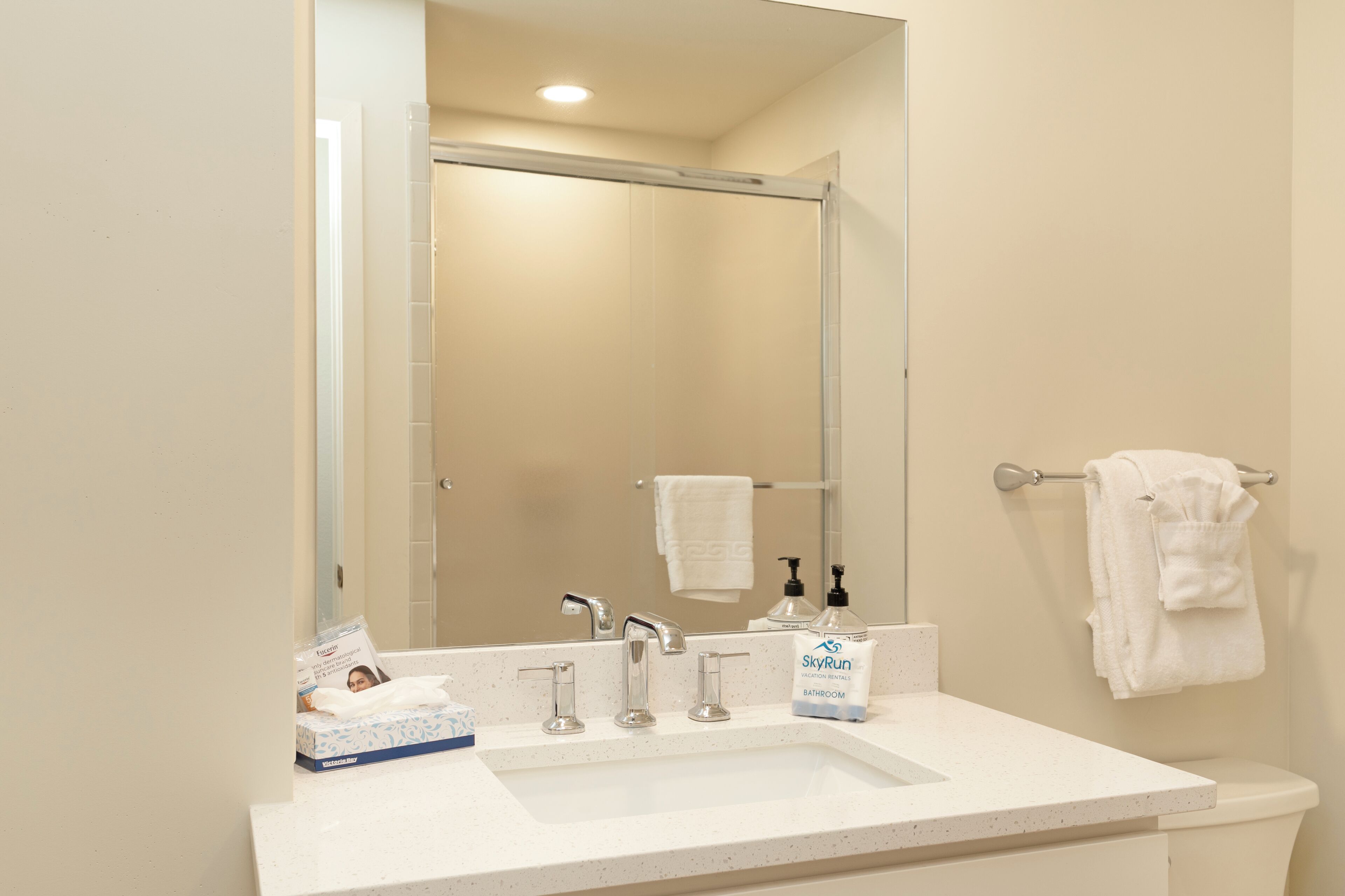 A bathroom with a white sink, three faucets, a mirror, and a towel rack with two towels.
