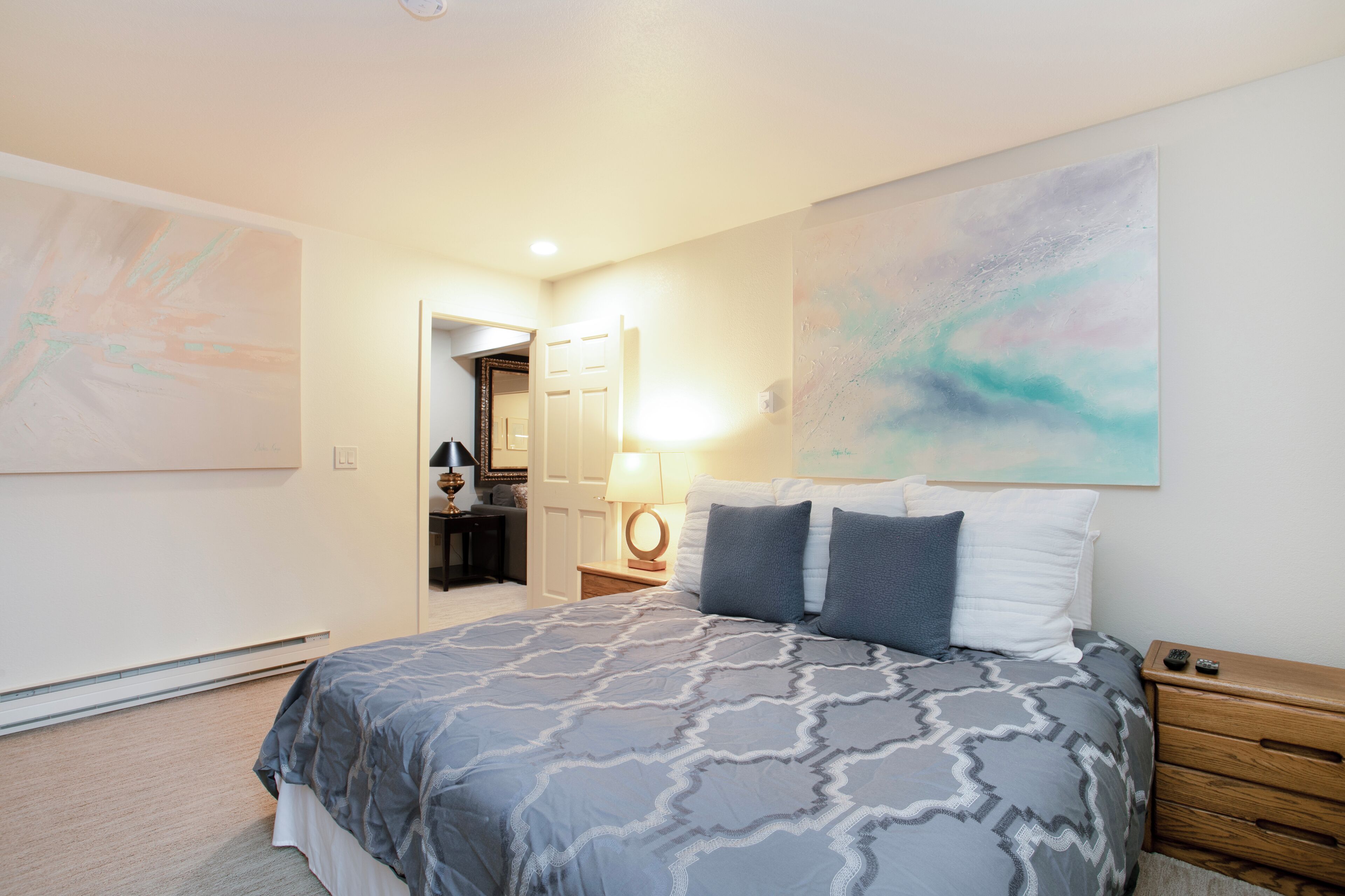 A bedroom with a bed, a nightstand, a lamp, and a door leading to another room.