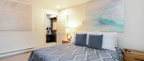 A bedroom with a bed, a nightstand, a lamp, and a door leading to another room.