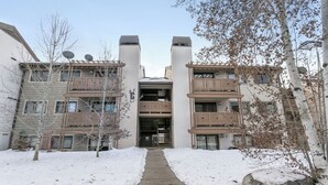 Un edificio residenziale a più piani con balconi, un ingresso centrale e un vialetto coperto di neve.