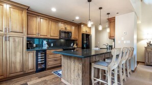 A kitchen with wooden cabinets, a central island with bar stools, a microwave, a refrigerator, and pendant lighting. - Beautiful Mountain Residence, Ski in/out, Year-Round Pool and Hot Tubs (Beaver Creek)