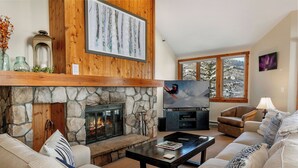 A cozy living room with a stone fireplace, a large TV, and comfortable seating. - Beautiful Mountain Residence, Ski in/out, Year-Round Pool and Hot Tubs (Beaver Creek)