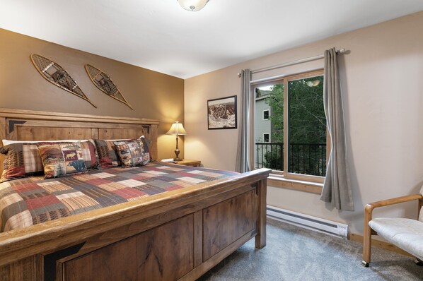 A bedroom with a wooden bed, a nightstand, a lamp, a window with curtains, and a chair. - Pool, Hot Tub, Complimentary Shuttle to Slopes, Great Location! (Avon)