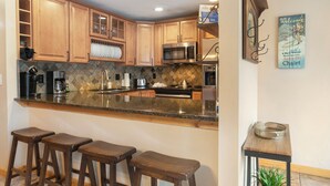 A kitchen with wooden cabinets, a granite countertop, a microwave, a coffee maker, and a bar stool area.