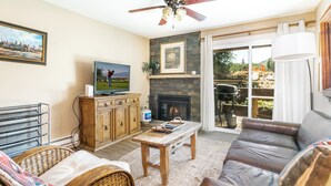Un salon avec une cheminée, un téléviseur et un ventilateur de plafond.