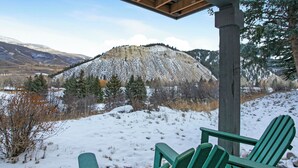 Een besneeuwd landschap met een houten constructie en groene Adirondack stoelen.