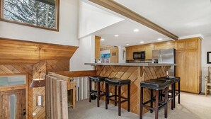 Een moderne keuken met houten details, een centraal eiland met barkrukken en een grote koelkast.
