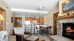 A living room with a fireplace, a dining area, and a kitchen in the background.