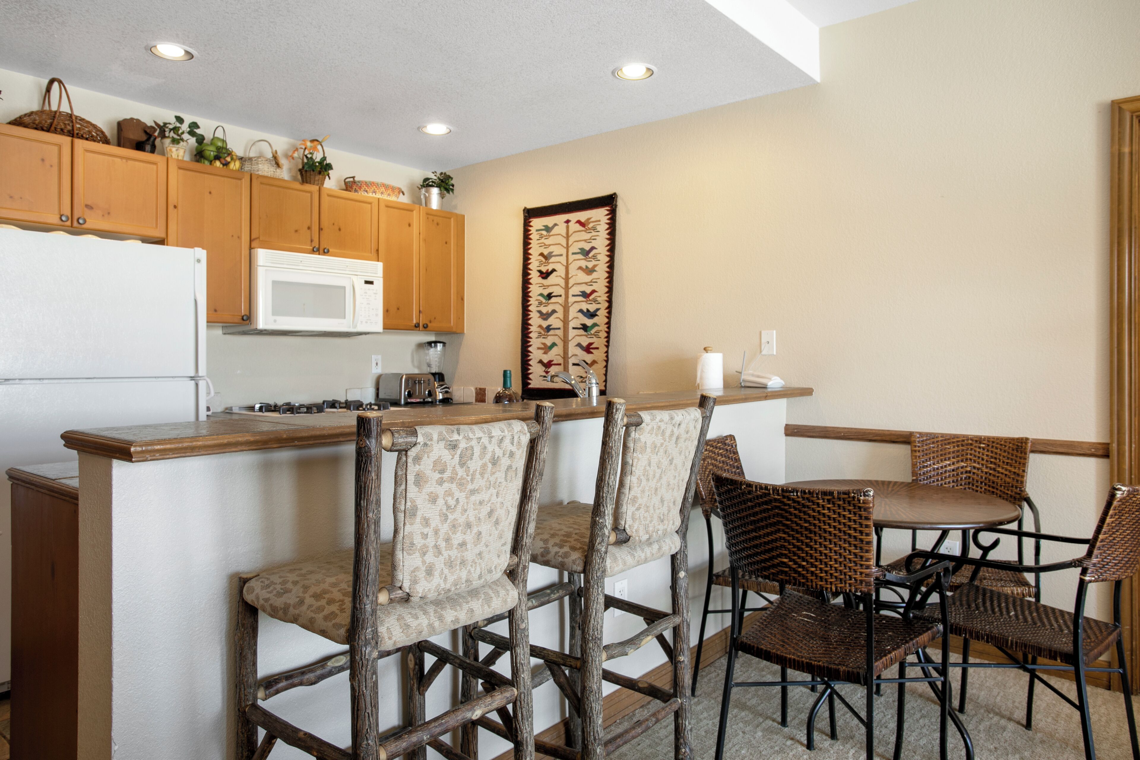 A kitchen with wooden cabinets, a microwave, and a bar area with wicker chairs.