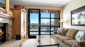 A cozy living room with a fireplace, a sofa, and a view of a snowy mountain.