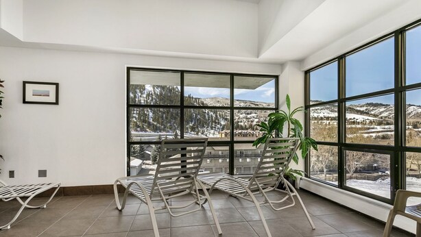 A room with large windows offering a view of a snowy landscape. There are two rocking chairs and a potted plant.
