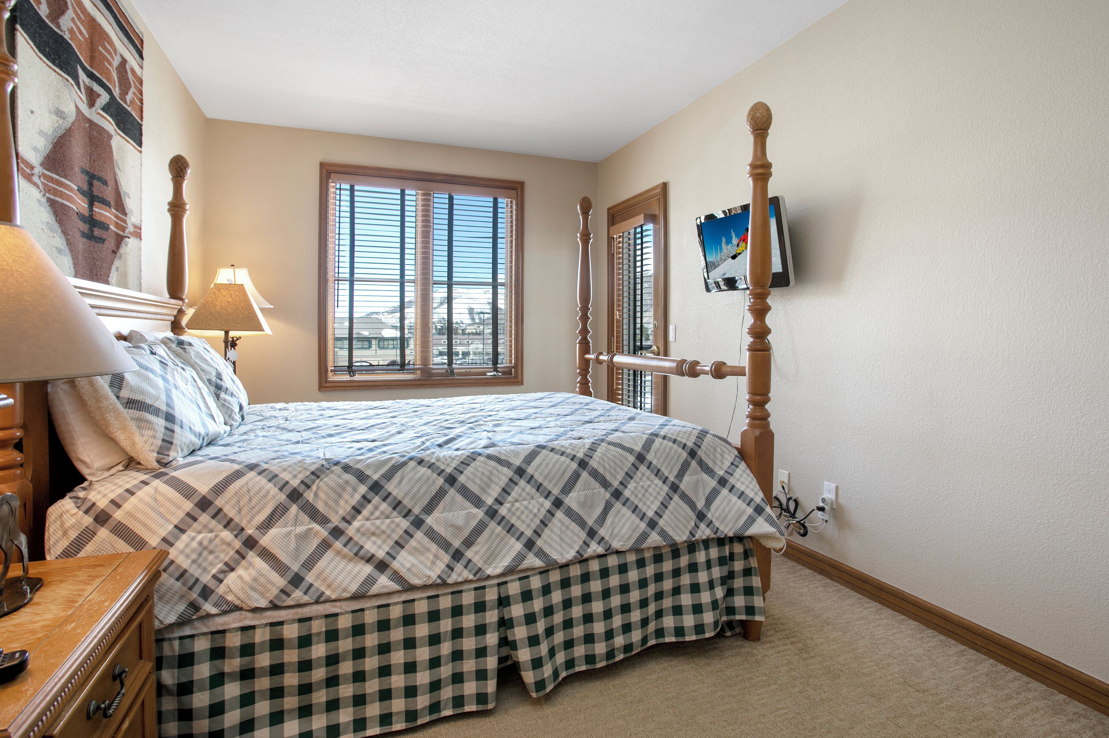 A bedroom with a bed, a dresser, a lamp, a window with blinds, and a painting on the wall.
