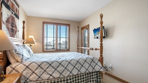 A bedroom with a bed, a dresser, a lamp, a window with blinds, and a painting on the wall.