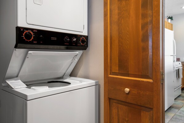 Una lavadora de carga frontal con un panel de control, una puerta de madera y un refrigerador blanco al fondo.
