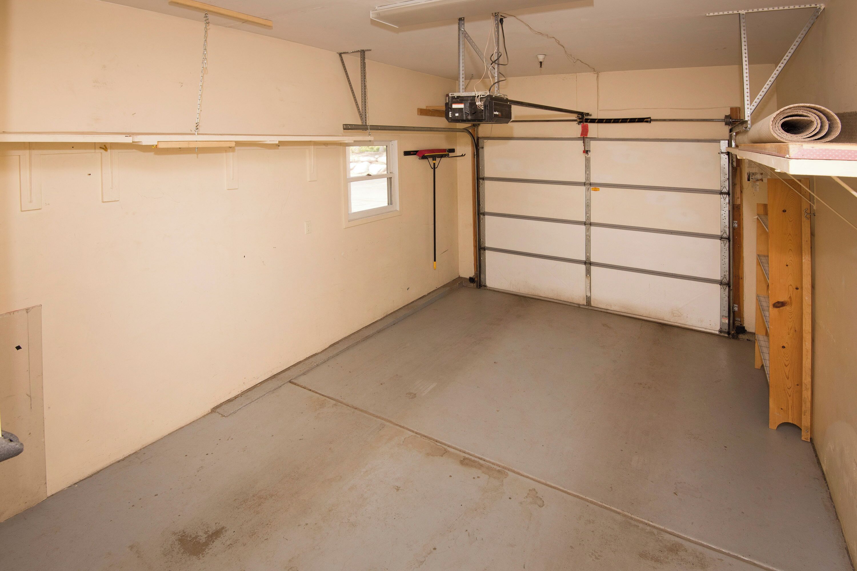 Un garage avec un sol en béton, une étagère en bois, une fenêtre et une porte de garage.
