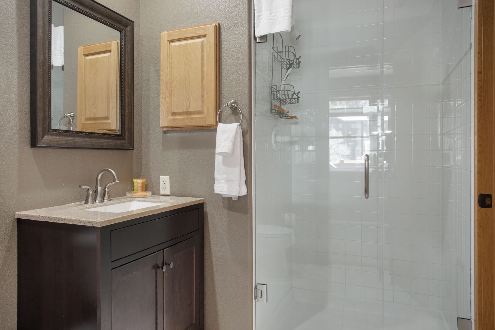 Une salle de bain avec un lavabo, un miroir, des meubles en bois et une cabine de douche en verre.