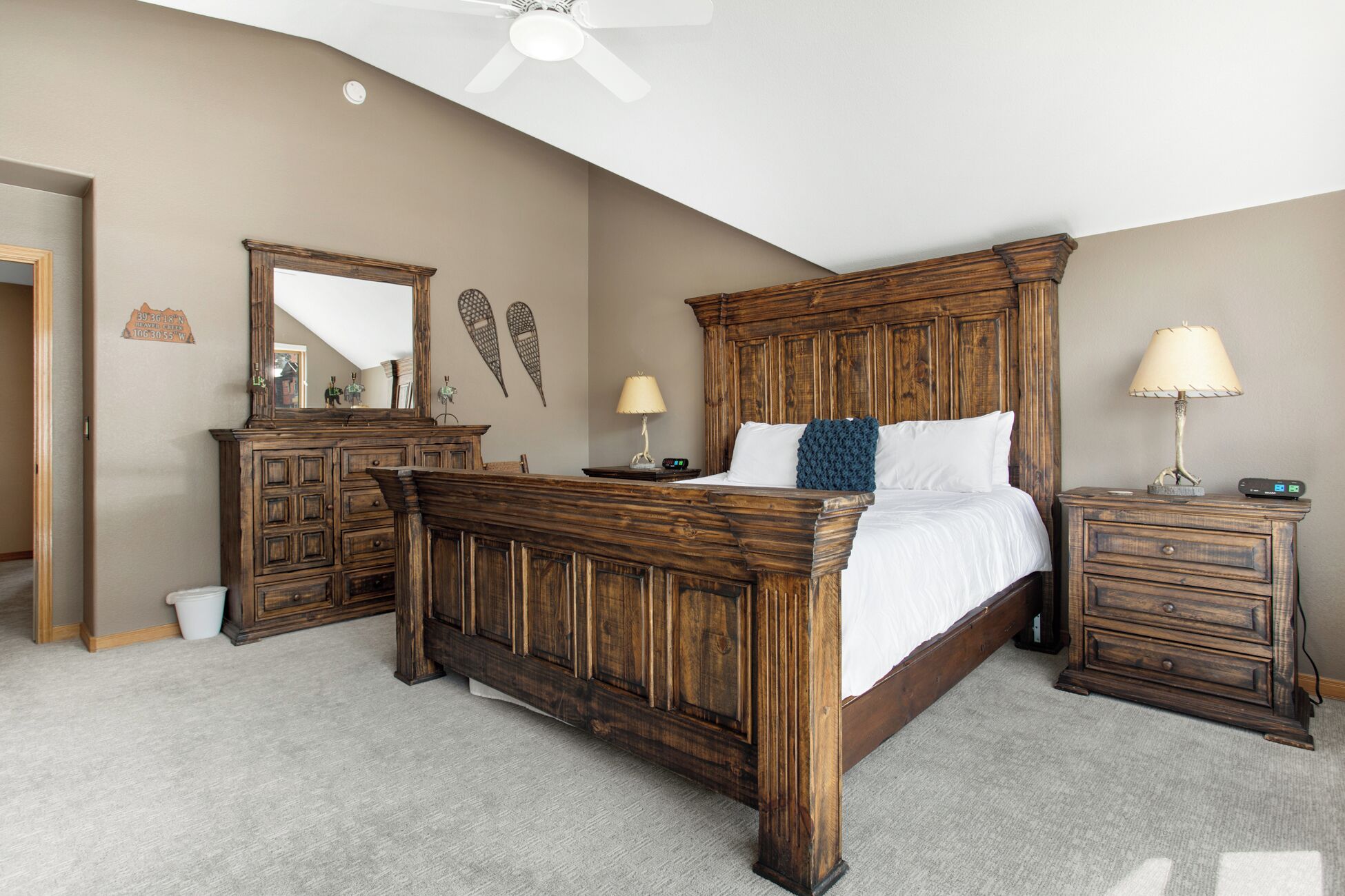 A bedroom with a wooden bed, two bedside tables, a nightstand, a dresser, a mirror, and a ceiling fan.