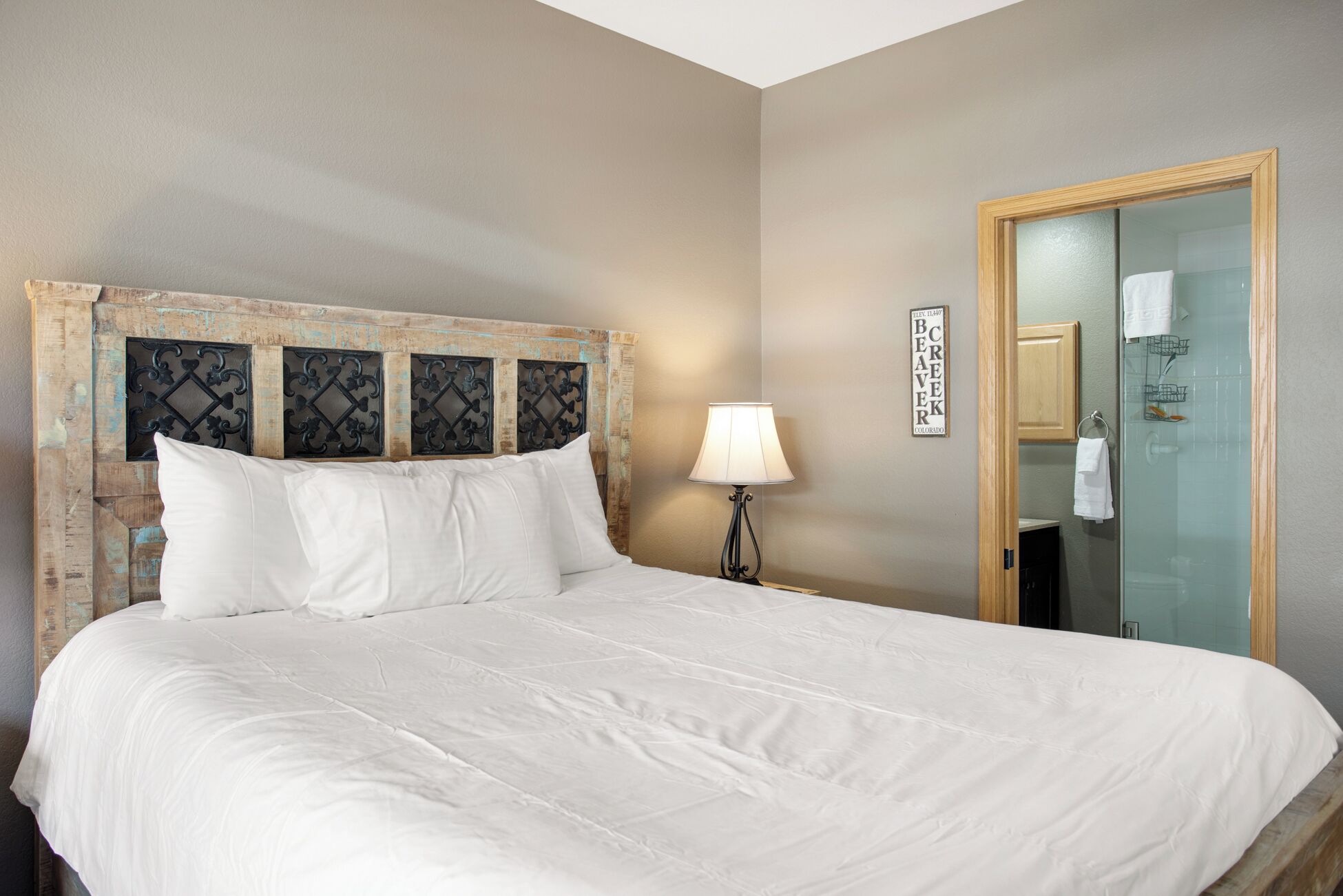 A hotel room with a bed, a nightstand with a lamp, a wooden headboard, a glass shower enclosure, and a sign on the wall.