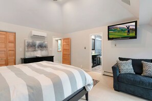 Ein Schlafzimmer mit einem Bett, einem an der Wand montierten Fernseher, einem Holzschrank und einem dunkelgrauen Sofa.