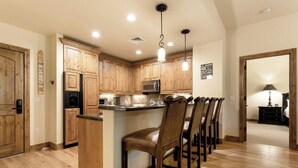 A kitchen with wooden cabinets, a microwave, and a bar area with chairs.