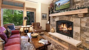 A cozy living room with a stone fireplace, comfortable seating, and a television mounted above it.