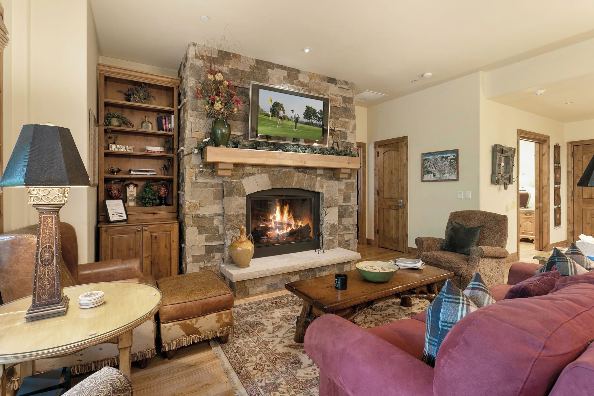 A living room with a stone fireplace, a television mounted above it, a bookshelf, and a comfortable seating area with a couch and armchairs.