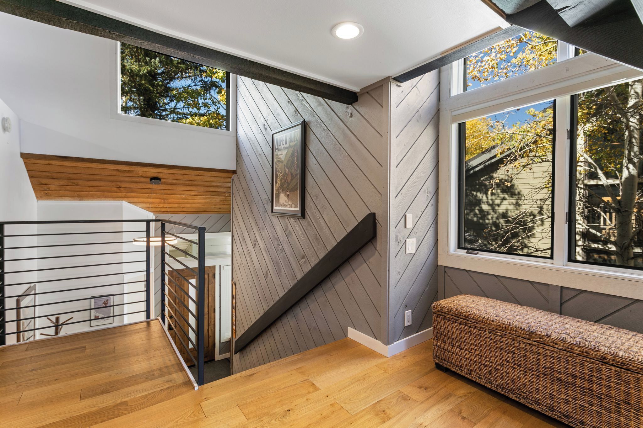 A modern interior with a wooden staircase, a bench, and large windows offering views of trees.